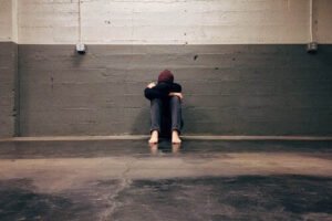 person sitting on the ground against a brick wall with head resting on top of knees
