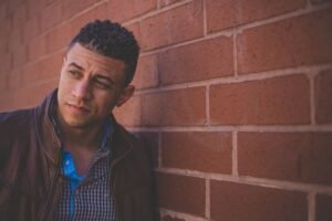 photo of a man leaning against a brick wall looking at something off camera