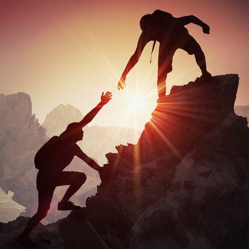 silhouette of person helping someone else up a mountain